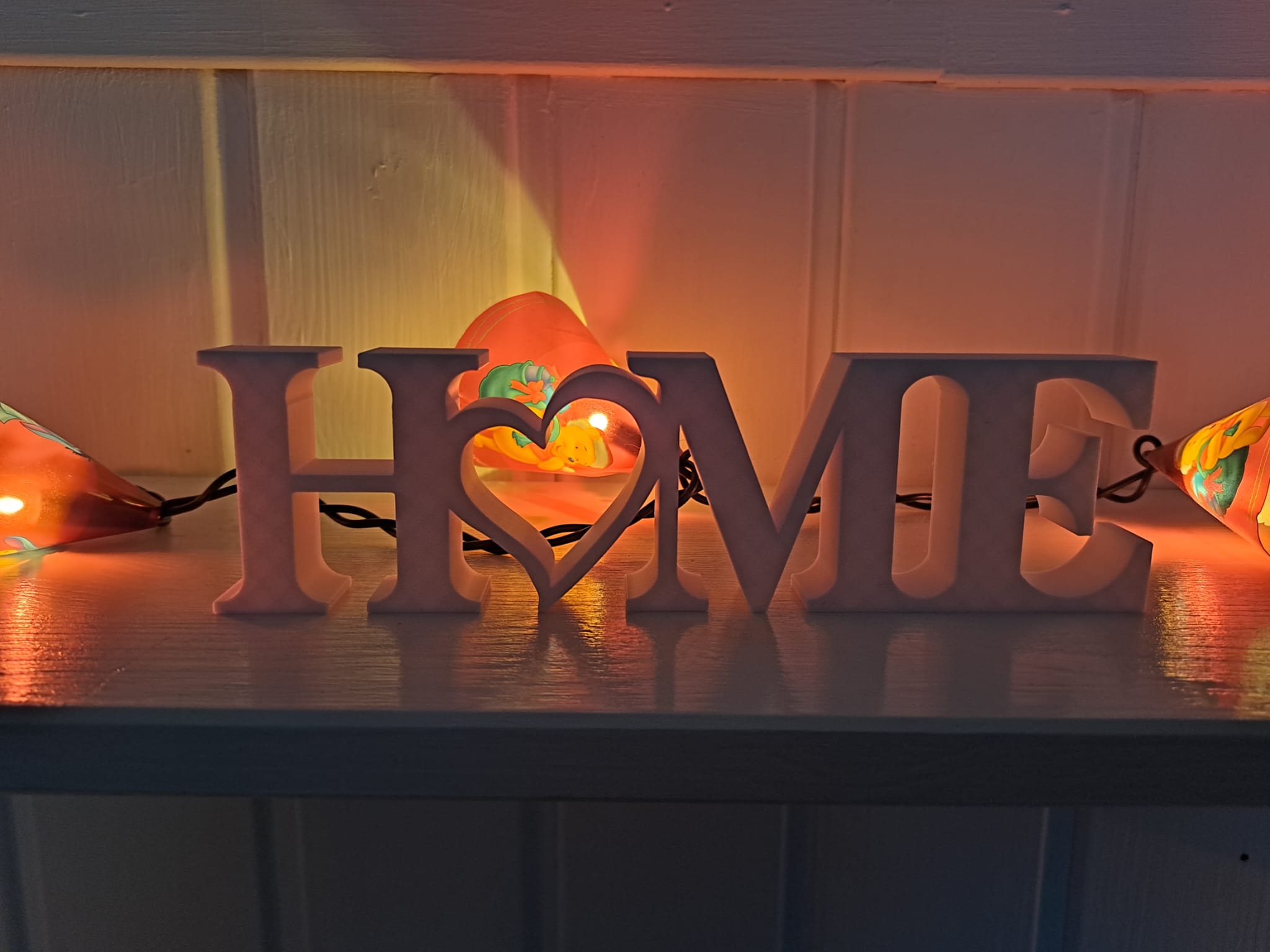 Valkoinen HOME-koriste lämpimän oranssin valosarjan edessä hämärässä.
