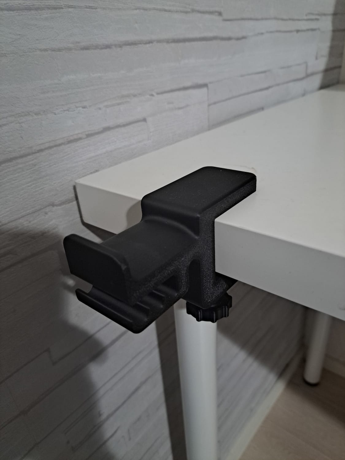 Musta kuuloketeline kiinnitettynä valkoisen pöydän reunaan.
